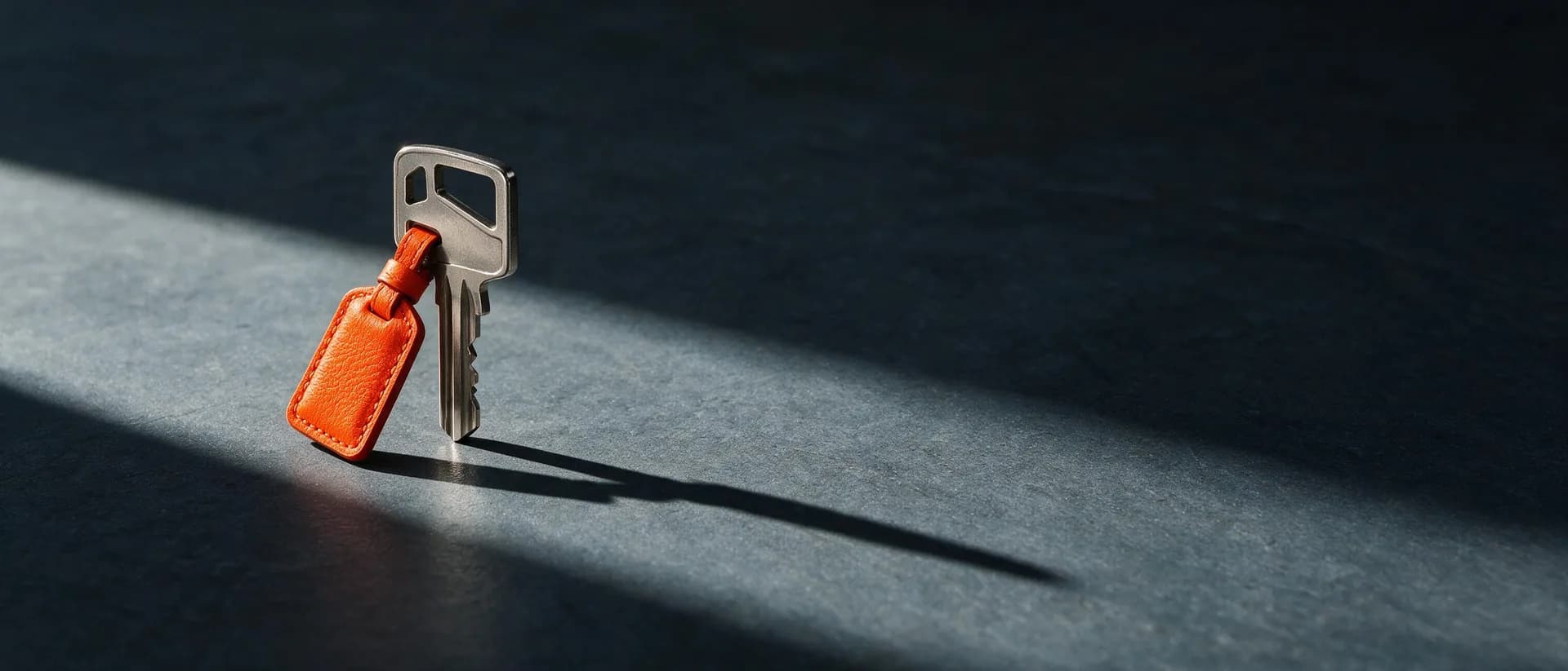 A single key standing upright with a terracotta tag, casting a long shadow