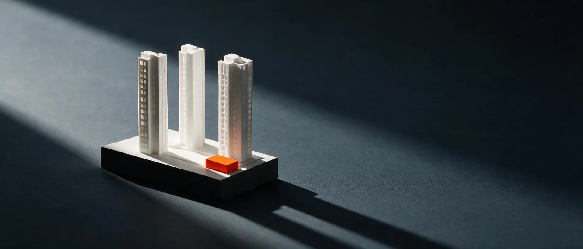 A white architectural scale model of three residential towers, marked with a terracotta pin