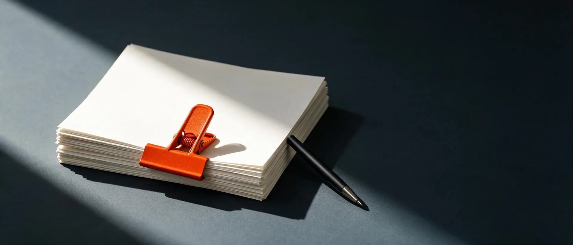 A neat stack of documents held by a terracotta clip beside a pen